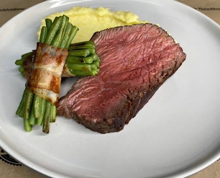 Rinderfilet mit Speckbohnen und Püree auf weißem Teller.
